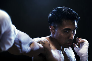 Portrait of determined kickboxer practicing against black background - CAVF28155