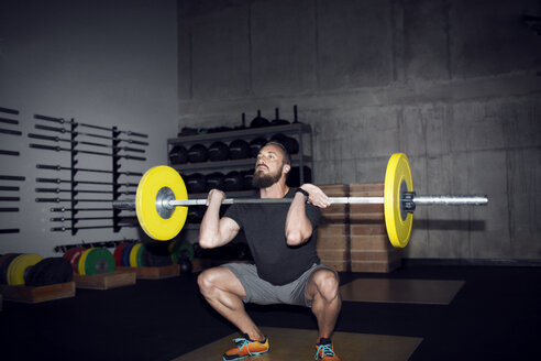 Entschlossener Sportler beim Heben einer Langhantel im Fitnessstudio in der Hocke - CAVF28162