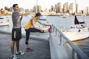 Male and female athletes doing stretching exercises on pier by harbor - CAVF28212