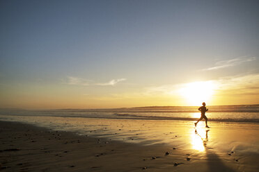 Seitenansicht eines männlichen Sportlers, der bei Sonnenuntergang am Strand läuft - CAVF28236