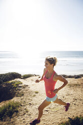 Glückliche sportliche Frau läuft am Strand - CAVF28243