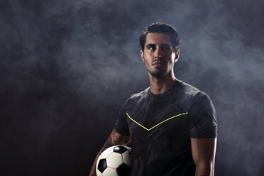 Thoughtful soccer player standing against black background - CAVF28259