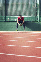 Tired sportsman sitting on retaining wall at field - CAVF28269