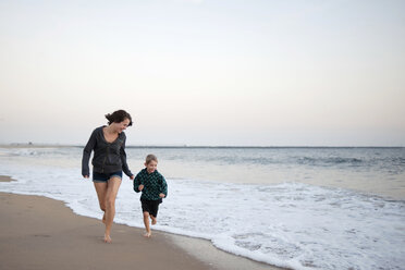 Mutter und Sohn laufen am Strand gegen den Himmel bei Sonnenuntergang - CAVF28329