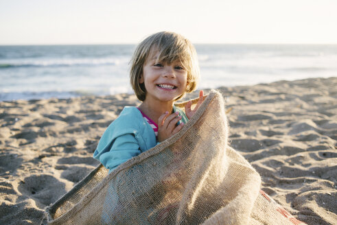 Porträt eines in einem Sack am Strand sitzenden Mädchens - CAVF28340