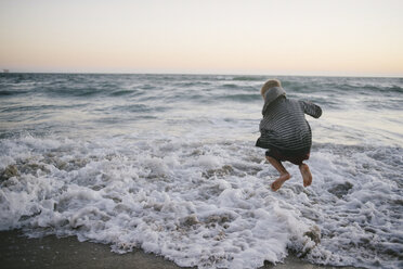 Rückansicht eines Jungen, der am Strand gegen den Himmel auf das Ufer springt - CAVF28342