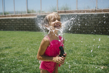 Cheerful girl splashing water on face with garden hose - CAVF28348