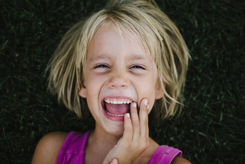 Overhead-Porträt eines fröhlichen Mädchens, das im Gras liegt - CAVF28364