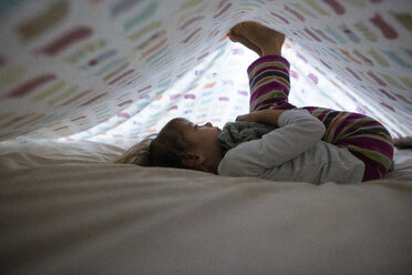 Side view of girl playing while lying underneath blanket at home - CAVF28368