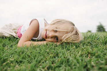 Portrait of cute girl lying on grassy field against clear sky - CAVF28370
