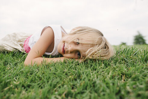 Porträt eines niedlichen Mädchens, das auf einer Wiese vor einem klaren Himmel liegt - CAVF28370
