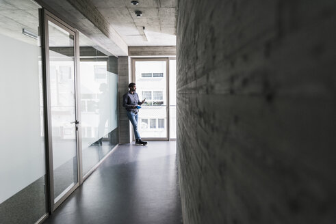 Geschäftsmann, der am Fenster steht und ein Mobiltelefon hält - UUF13085