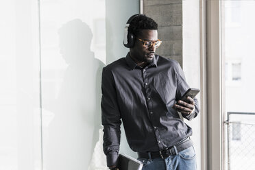 Businessman wearing headphones looking at cell phone - UUF13087