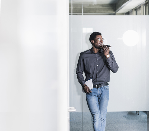 Happy businessman standing at glass pane using smartphone stock photo