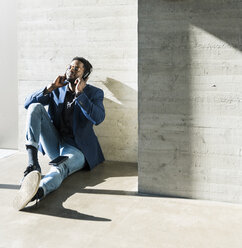 Businessman sitting on the floor in sunshine wearing headphones - UUF13096