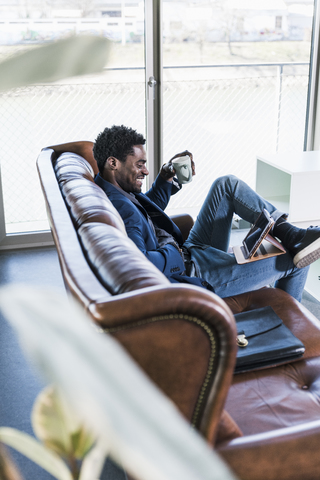 Lächelnder Geschäftsmann sitzt auf der Couch und benutzt ein Tablet, lizenzfreies Stockfoto