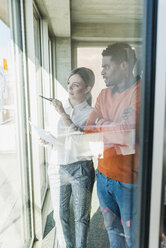 Casual businesswoman and businessman discussing paper at the window - UUF13112