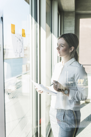 Junge Geschäftsfrau betrachtet Papier am Fenster, lizenzfreies Stockfoto