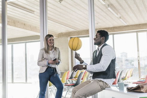 Frau schaut auf Geschäftsmann, der im Büro einen Basketball balanciert - UUF13118