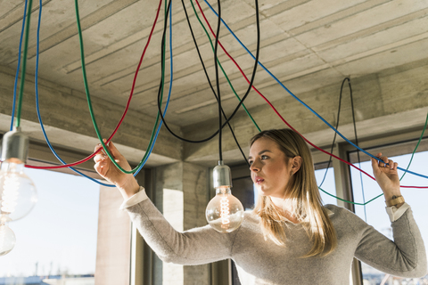 Junge Geschäftsfrau im Büro, die Kabel an Glühbirnen untersucht, lizenzfreies Stockfoto