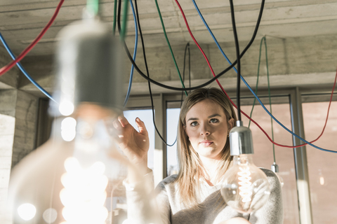 Young businesswoman in office examining cables at light bulbs stock photo