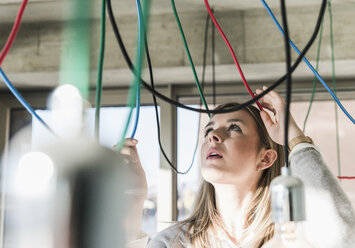 Young businesswoman in office examining cables at light bulbs - UUF13128