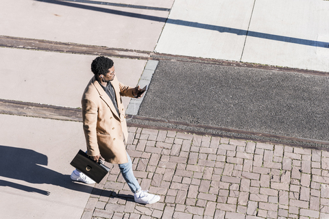 Businessman walking outdoors with briefcase, cell phone and earphones stock photo