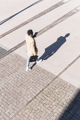 Businessman walking outdoors with briefcase, cell phone and earphones - UUF13140