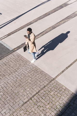 Businessman walking outdoors with briefcase, cell phone and earphones stock photo