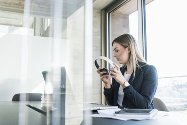 Young businesswoman with laptop and headphones working at desk in office - UUF13153