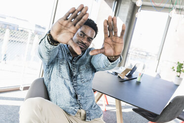 Portrait of smiling casual businessman in office making a finger frame - UUF13158