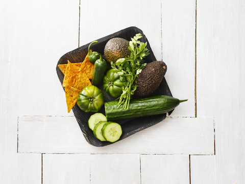 Wooden bowl of avocados, green tomatoes, Jalapeno peppers, cucumber and tortilla chips stock photo