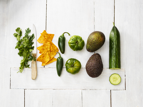 Avocados, green tomatoes, Jalapeno peppers, cucumber, parsley, kitchen knife and tortilla chips on white wood stock photo