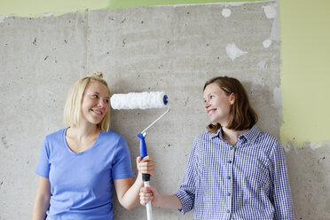 Young women standing by wall and holding paint roller - FOLF00035