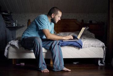 Mann sitzt auf dem Bett und benutzt einen Laptop - FOLF00052