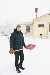 Mann steht mit rosa Schneeschaufel vor einem Haus - FOLF00111