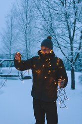 Junger Mann mit Weihnachtsbeleuchtung in der Abenddämmerung - FOLF00115