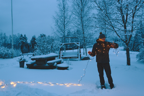 Junger Mann mit Weihnachtsbeleuchtung im Hinterhof in der Abenddämmerung, lizenzfreies Stockfoto