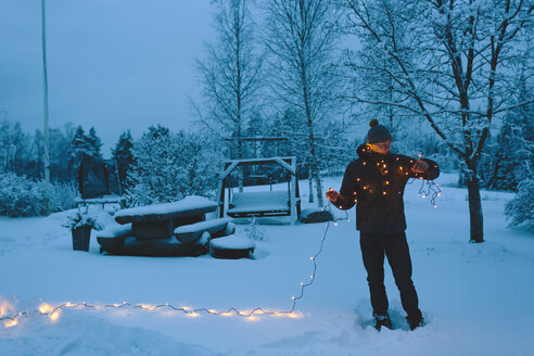 Young man holding Christmas lights in backyard at dusk - FOLF00116