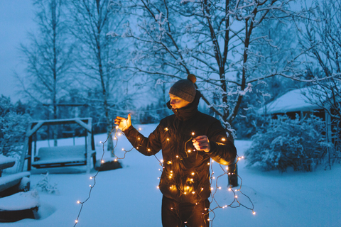 Junger Mann mit Weihnachtsbeleuchtung im Hinterhof in der Abenddämmerung, lizenzfreies Stockfoto