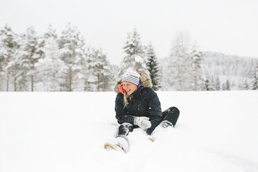 Lachende junge Frau im Schnee sitzend - FOLF00127