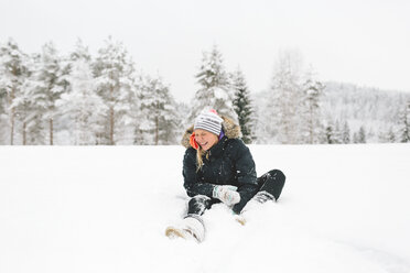 Laughing young woman sitting in snow - FOLF00127