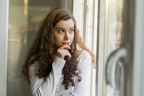 Teenager-Mädchen, das aus dem Fenster schaut und träumt, lizenzfreies Stockfoto