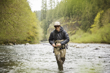 Front view of man walking with fishing rod on river - CAVF28373