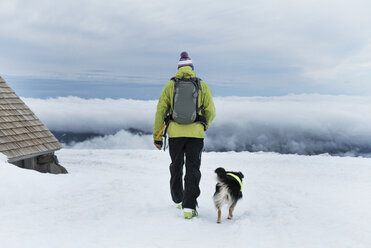 Rear view of man walking with dog on snow covered field - CAVF28379