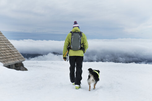 Rückansicht eines Mannes, der mit seinem Hund auf einem schneebedeckten Feld spazieren geht - CAVF28379