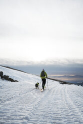 Man hiking with dog on snow covered field against cloudy sky - CAVF28380