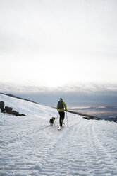 Mann wandert mit Hund auf schneebedecktem Feld gegen bewölkten Himmel - CAVF28380