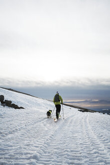 Mann wandert mit Hund auf schneebedecktem Feld gegen bewölkten Himmel - CAVF28380