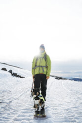 Man standing with dog on snow covered field during hiking - CAVF28382